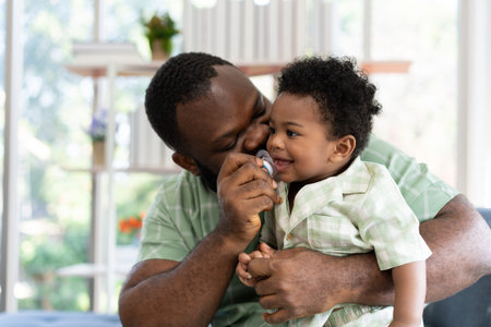 Happy african american man play with little infant toddler child in living room sofa. Parent and...