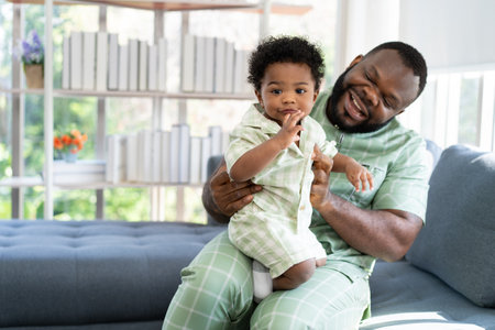 Happy african american man play with little infant toddler child in living room sofa. Parent and little kid relaxing at home. Parents and toddler child girl enjoying spending time at home. Childcareの写真素材