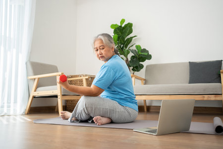 Asian senior woman lifting dumbbell for exercise and workout at home. Active mature woman doing stretching exercise in living room. Exercise Active and healthy for older, elder, and senior concept.の写真素材