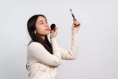Beautiful young woman makes blush on her face using makeup brush on isolated white background. Teenage girl doing her own makeup. Close up portrait. Copy, empty space for textの写真素材