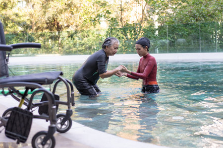 Selective focus off wheelchair background of physical therapist helping senior woman in aqua, old women and mature doing aqua aerobics exercise in swimming pool, Elderly sports, and active lifestyle.の写真素材