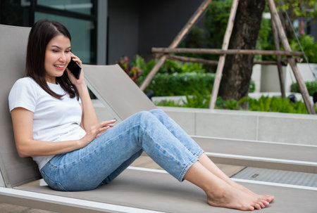 Young Asian woman freelancer traveler working online using smartphone and sitting at poolside while traveling on vacation. Work on vacation,  Freelance and workstation conceptの写真素材