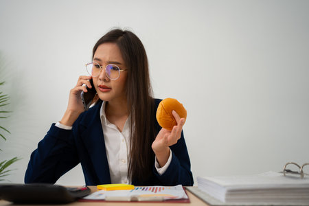 Busy and tired businesswoman eating Bread and milk for lunch at the Desk office and working to deliver financial statements to a boss. Overworked and unhealthy for ready meals, burnout concept.の写真素材