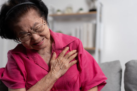 Asian senior elderly grandmother suffering from heart pain and holding her chest while sitting on...