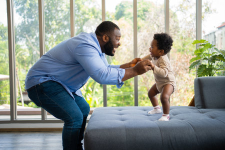 Portrait Of Happy African American Dad With Cute Little Baby Girl on couch at home in the living room, caring father smiling and amusing his girl while sitting on the couch, happy familyの写真素材