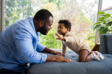 Portrait Of Happy African American Dad With Cute Little Baby Girl on couch at home in the living room, caring father smiling and amusing his girl while sitting on the couch, happy familyの写真素材