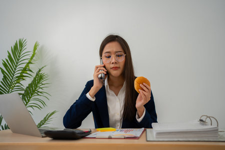 Busy and tired businesswoman eating Bread and milk for lunch at the Desk office and working to deliver financial statements to a boss. Overworked and unhealthy for ready meals, burnout concept.の写真素材