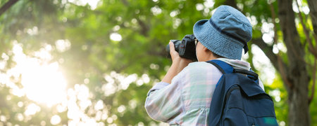 Portrait of Asian mature woman holding a camera and backpack behind her back, an Asia active senior woman enjoying nature in park. Standing on a trail in a forest outdoors. Enjoying active travel tripの写真素材