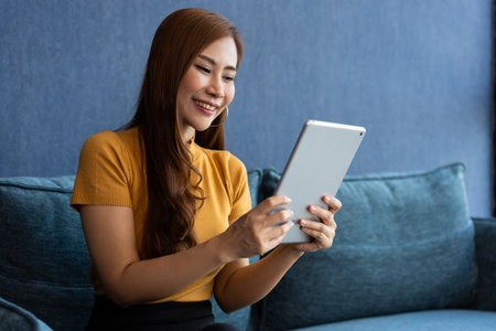 Portrait of Young attractive asian woman resting on sofa and using and looking at tablet pc in modern room communication and lifestyle concept. reading digital gadget at house.の写真素材