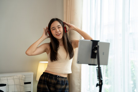 Asian women and beautiful bloggers wear headphones dancing videos by smartphone cameras. Creator vlogger talent dancing enjoys hobby content recording show video sharing on social media.の写真素材