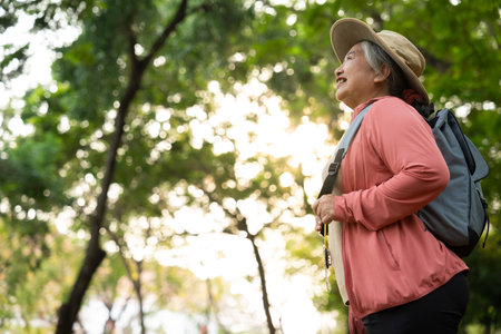 Portrait of Asian mature woman in a hat with backpack behind her back, an Asia active senior woman enjoying nature in autumn park. Standing on a trail in a forest outdoors. Enjoying active travel tripの写真素材