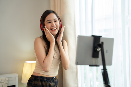 Asian women and beautiful bloggers wear headphones dancing videos by smartphone cameras. Creator vlogger talent dancing enjoys hobby content recording show video sharing on social media.の写真素材