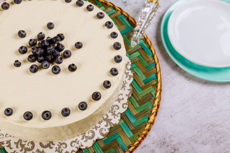Festive white cake with fresh blueberries and plates on a white background.