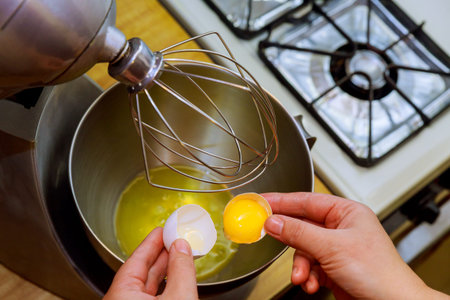 Woman breaks an egg in a metal bowl. Separate egg white from yolk.