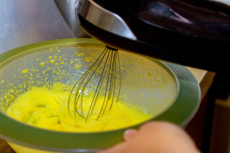 Mixing egg yolk with sugar in bowl with electric mixer.