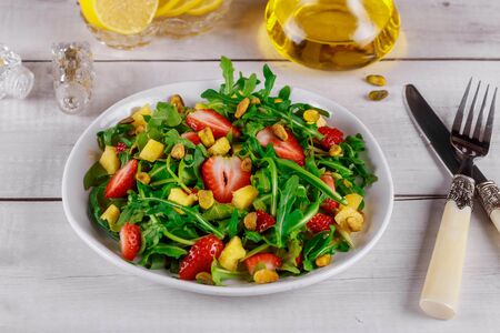 Fresh salad with arugula, strawberries, pineapple and pistachios served on white plate on rustic wooden table. Organic concept.の写真素材