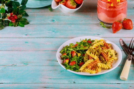 Tricolor rotini pasta from durum wheat with green salad on wooden blue table.