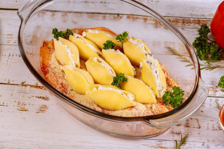 Staffed jumbo shells pasta in glass baking pan on white woodwn background.の写真素材