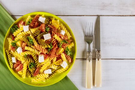 Rotini pasta and cherry tomato with green salad on wooden table with knife and fork.の写真素材