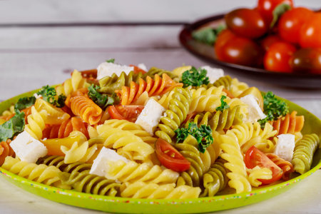 Italian colorful pasta rotini with cut cherry tomatoes on white wooden background.の写真素材