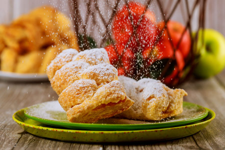 Powdered sugar sprinkle on apple strudel with fresh apples in wire basket.