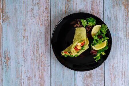 Spinach wrap with meat and vegetables on black plate with green salad and lemon.の写真素材