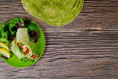Wrap with grilled chicken and vegetable on spinach green tortillas on wooden table.の写真素材