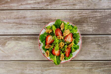 Spinach salad with strawberry, walnuts and sesame seeds on wooden background.の写真素材