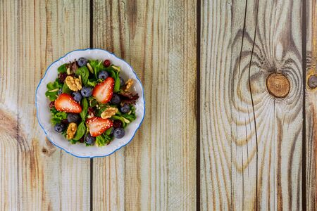 Delicious spinach salad with strawberry, walnuts and sesame seeds on wooden background.の写真素材