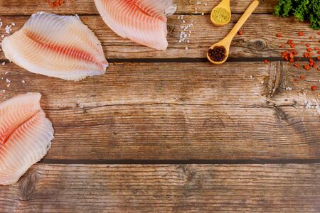 Raw fillet of tilapia with spices and herbs on rustic wooden background top view.の写真素材