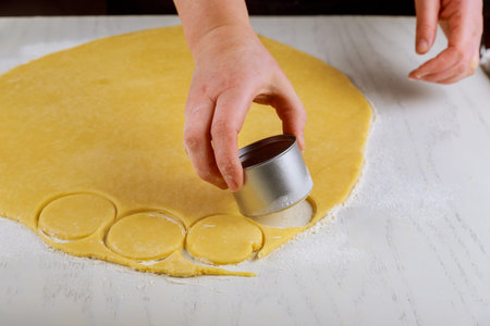 Woman cuts dough for baking cookies on white table.