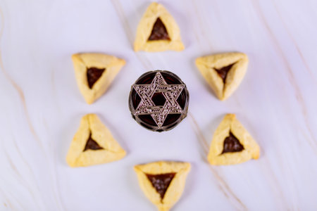 Star of David on glass with wine and blurry purim cookies not in focus.