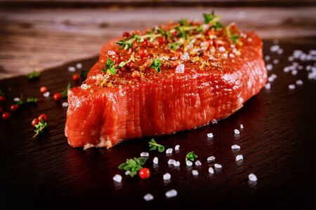 Fresh beef tenderloin with herb, salt and peppercorn over black stone board.の写真素材