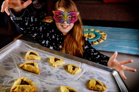 Jewish girl with long hair has fun and dancing in mask with cookies on Purim holiday.の写真素材