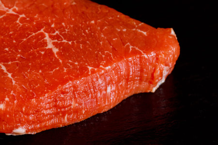 Uncooked marble beef tenderloin over black stone board.