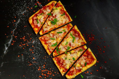 Cut into slices hawaiian pizza with ham, cheese and pineapple on a dark background. Top view.