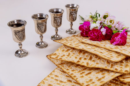 Jewish matzah bread on wooden rustic background with four wine cups and flowers. Passover holiday...