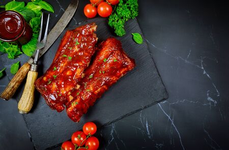 Pork ribs grilled with BBQ sauce , tomato and spinach on black board.の写真素材