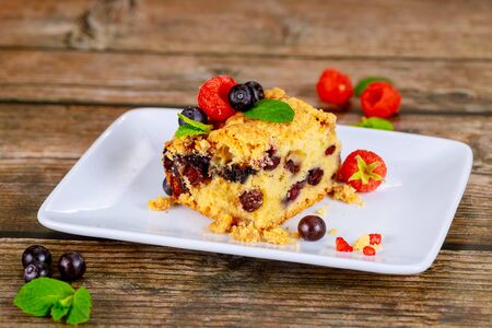 Piece of blueberry coffee cake with fresh berries on white plate on wooden background.の写真素材