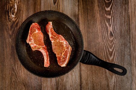 Raw bone in steak on the pan skillet on wooden background. Top view.の写真素材