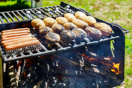 Potato skewers with sausage on burning coals and wood grill.の写真素材