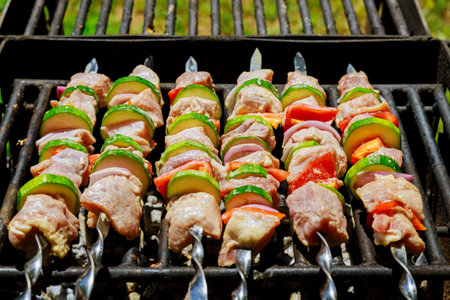 Skewers with marinated pork shish kebab and vegetables on grill.
