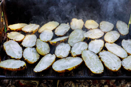 Grilling cut potatoes with butter on outdoor charcoal grill.の写真素材