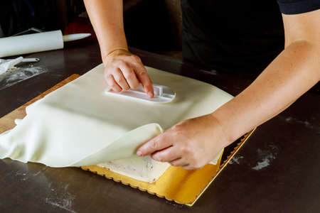 Baker covering square cake with white fondant. Technique of making wedding cake.の写真素材