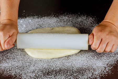 Rolling pin in woman hand and white sugar paste on table.