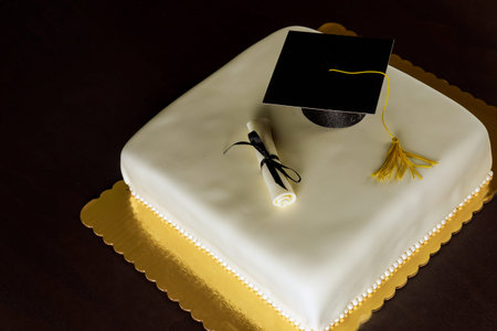 Graduation white cake with cap on the top and diploma decor.