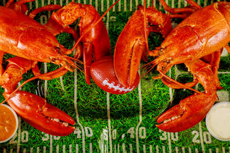 Two red cooked lobsters on green plate with football ball. American football concept.の写真素材