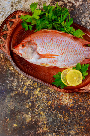 Fresh fish with herbs and lemon on tray. Top view.