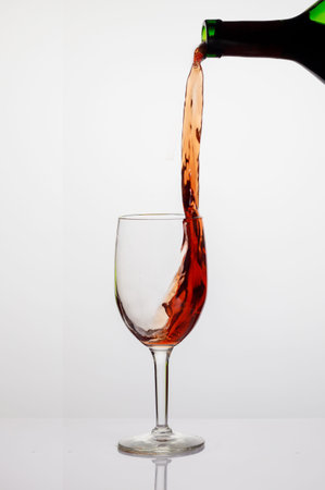 Pouring red wine into wine clear glass on white background.の写真素材