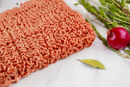 Close up of ground beef with onion, rosemary and bay leaf on white background.の写真素材